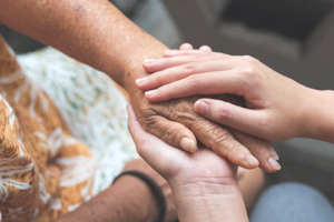 a caregiver holds the hand of a patient receiving palliative care to comfort them