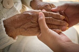 shot of nurse holding patient's hands while discussing end of life conversations with families