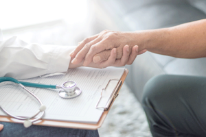 shot of clasped hands over medical chart while discussing the compassus financial assistance policy