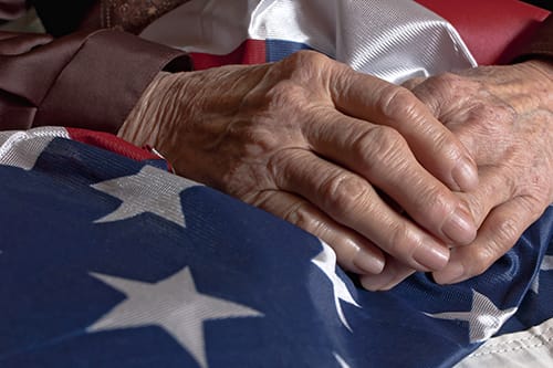 person with clasped hands over a flag considering the hospice benefit for veterans
