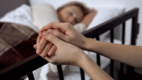person laying bed holds hand of hospice services provider