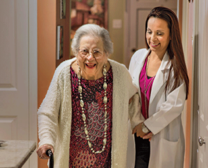 a doctor helps a senior woman with a cane walk through facility after doctor explained the differences between home health care vs personal care
