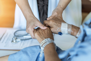 a palliative care team member comforts a patient by holding their hands and talking to them