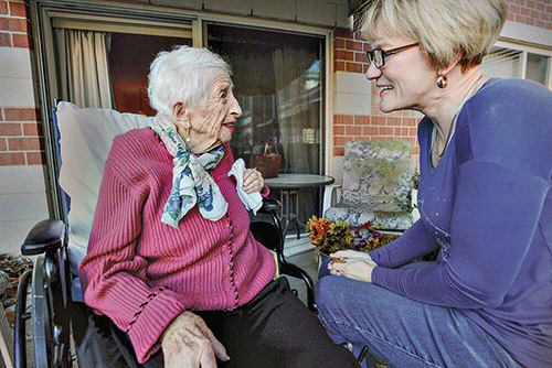 a senior woman sits with a woman visitor while senior woman talks about hospice resources for caregivers
