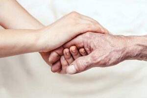 hospice chaplain holds the hand of a patient