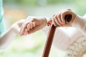 person with cane holds hand of a hospice social worker