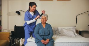 Nurse, brush and senior patient with hairstyle for self care, grooming or morning routine at assisted living. Healthcare, retirement home and caregiver help elderly woman with beauty treatment.