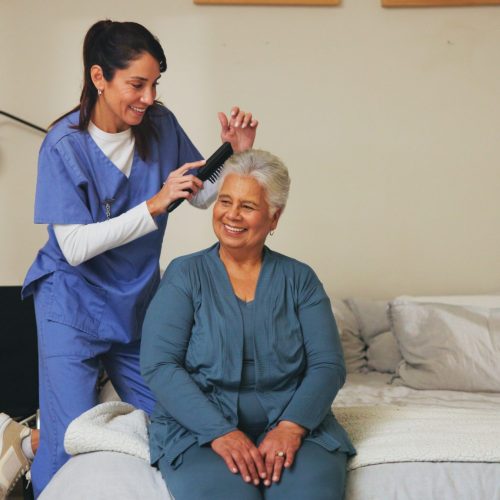 Nurse, brush and senior patient with hairstyle for self care, grooming or morning routine at assisted living. Healthcare, retirement home and caregiver help elderly woman with beauty treatment.